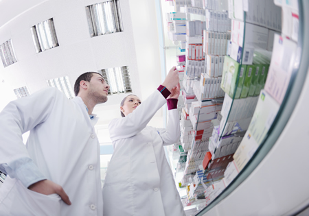 Two Pharmacy Technicians studying prescription packages on a shelf display