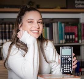 A female student smiling and holding a calculator in a library