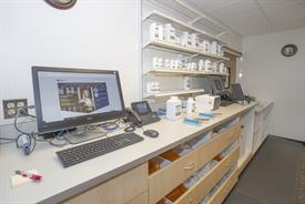 View of a pharmacy environment with a computer counter, shelves of bottles and many drawers