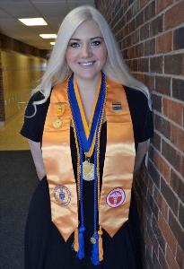 Steffanie Hills stands proudly in a college hall wearing various awards and honor cords 