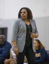 Head coach of the basketball team is standing during a game watching her players