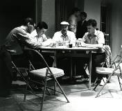 A stage scene of men playing cards at a table.